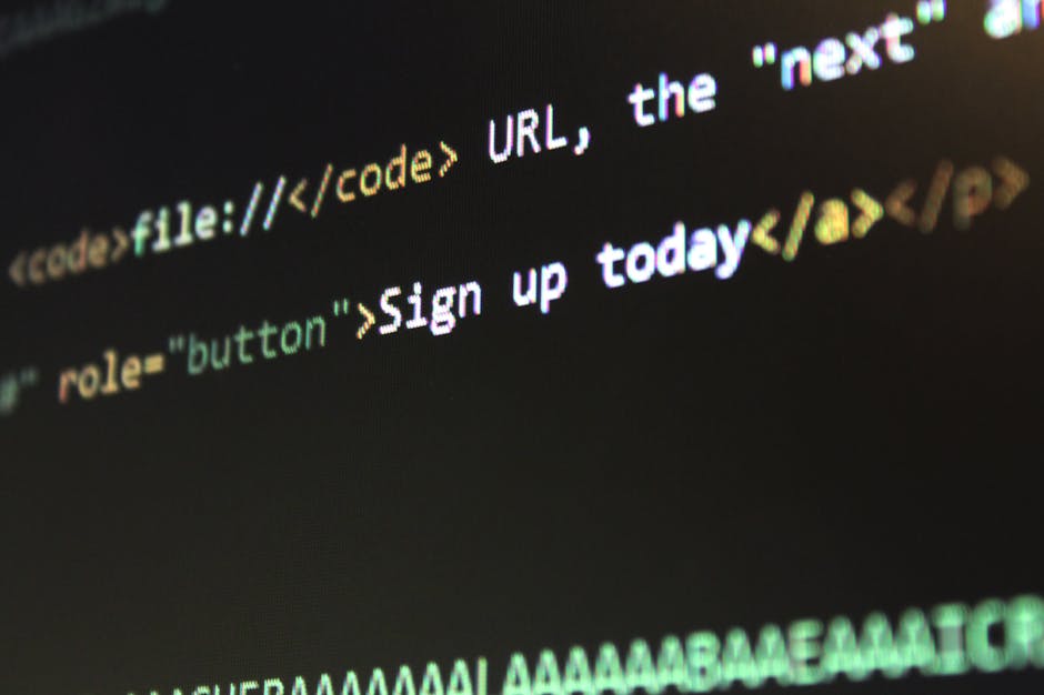 A close-up view of a person's hand wearing a silver wristwatch, working on a laptop placed on a wooden desk. The laptop screen displays lines of HTML or code in a text editor, with the background of t
